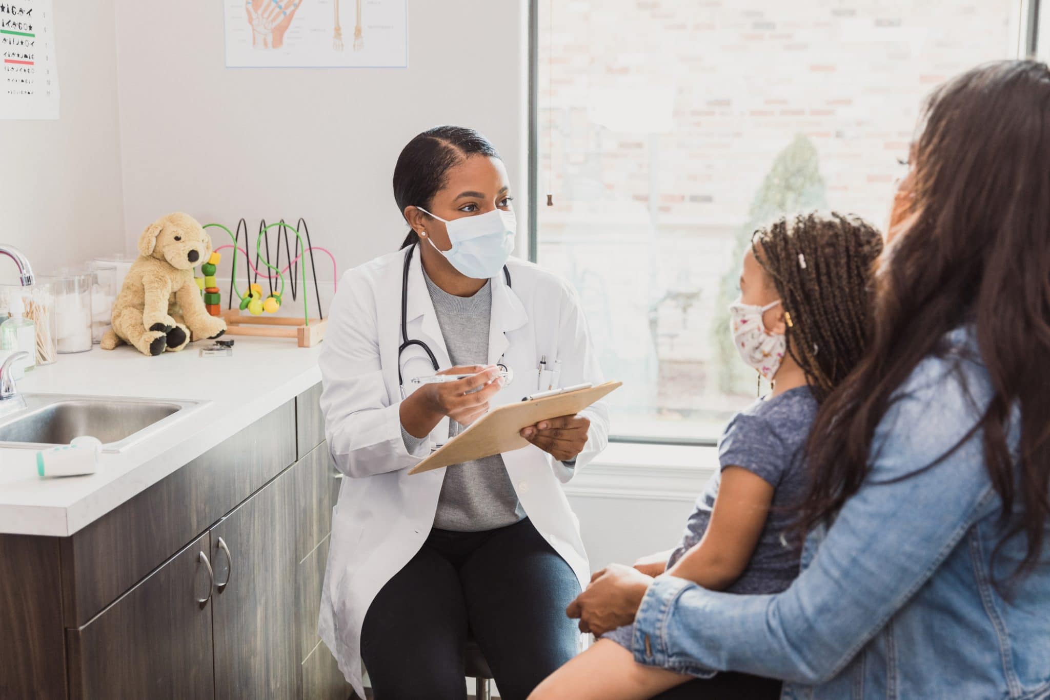 Female pediatrician talks with patient's mother With a protective mask on, a female pediatrician talks to a young patient's mother about the woman's daughter's medical conditions. They are wearing protective masks during the COVID-19 pandemic.