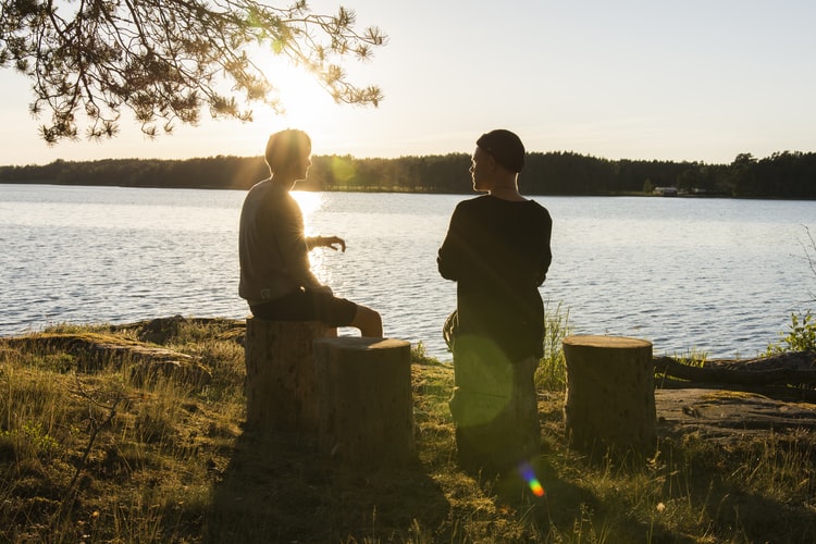 communication-hearing-loss Two people speaking outside near a lake.