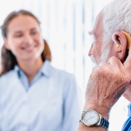 Older man with a hearing aid speaking to his audiologist/