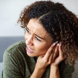 A woman experiencing severe tinnitus holds her hands to her ear.