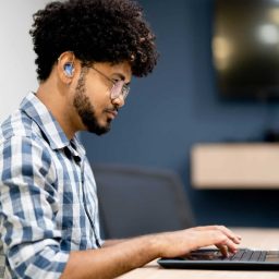 Side view of man with a hearing aid working on laptop at office