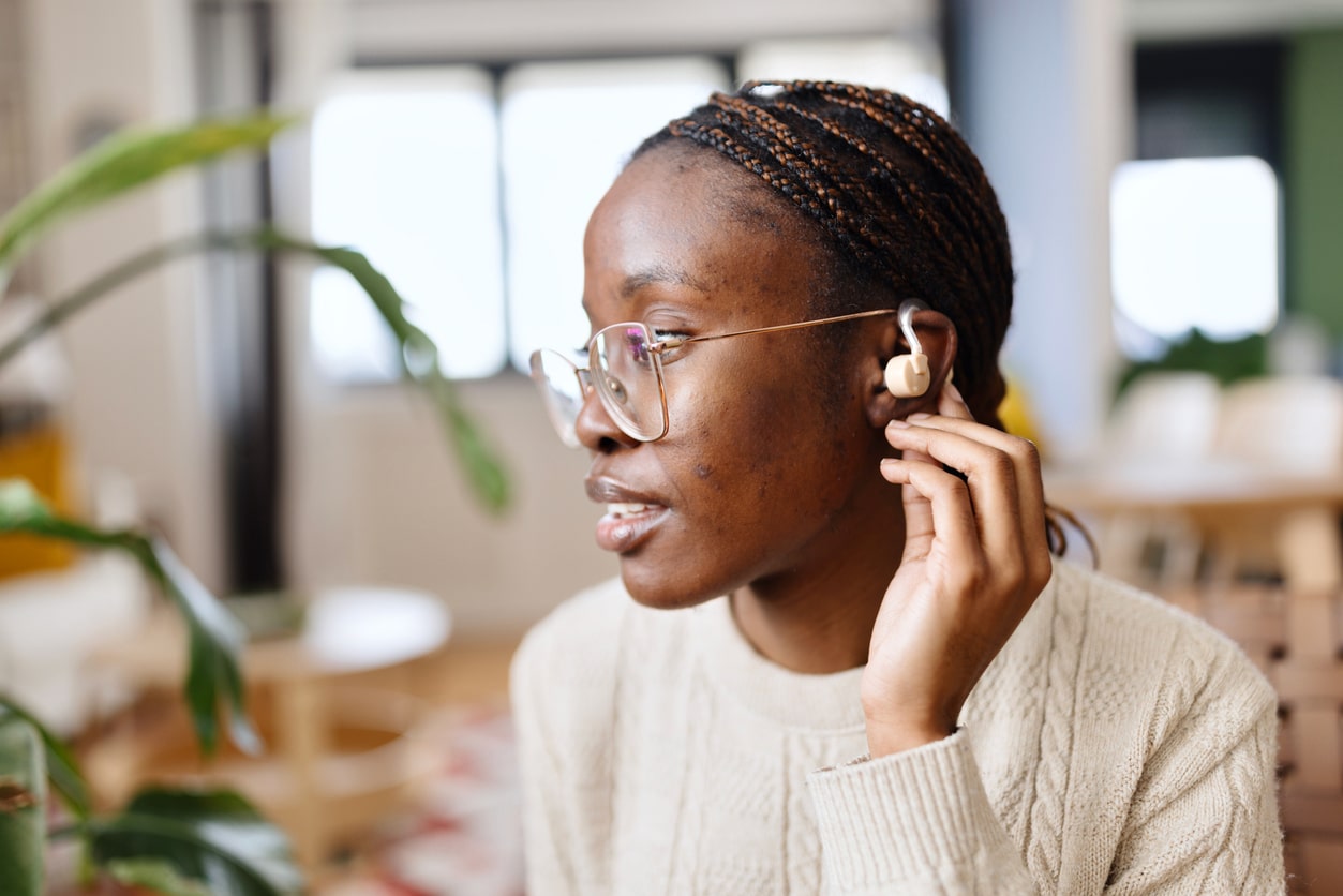 Woman touches hearing aid behind ear