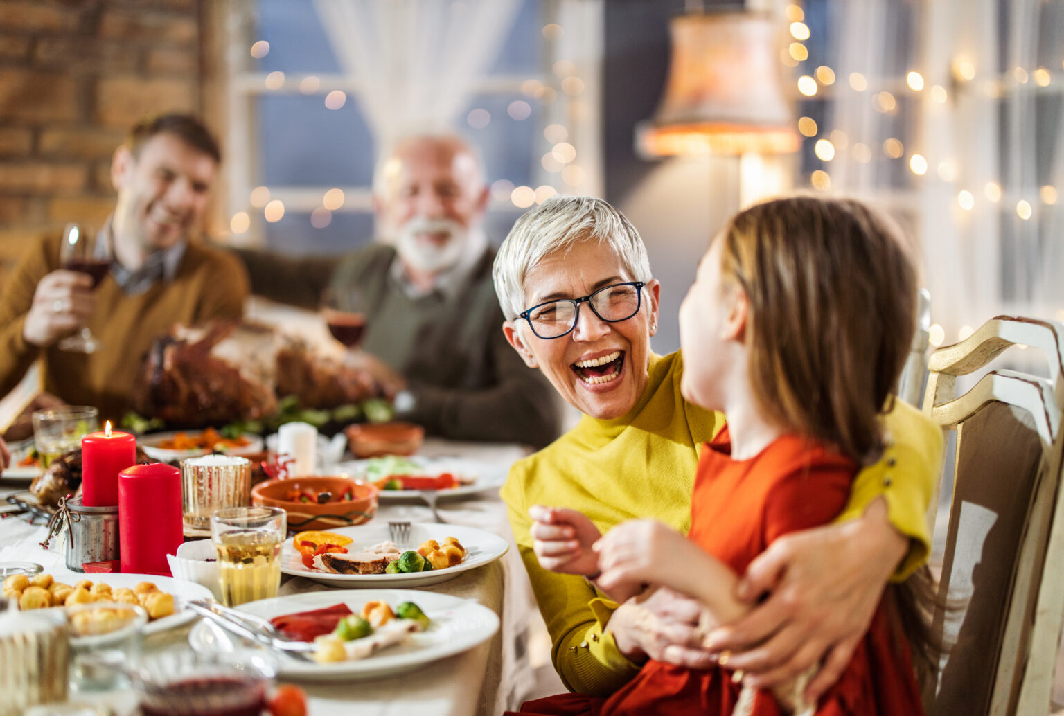 Happy holiday family dinner; an excited grandmother embraces her grandchild at a festive dinner table.