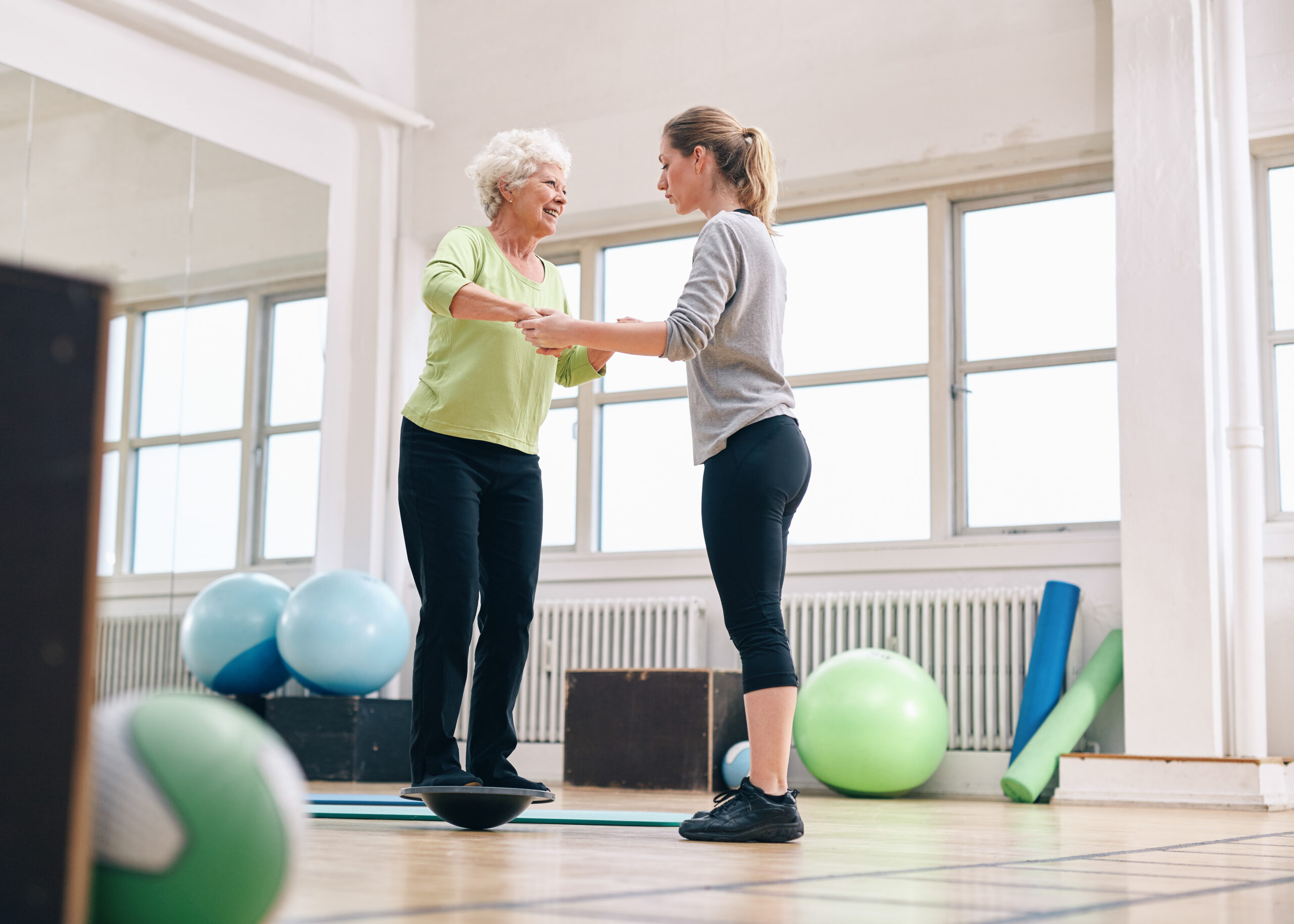 A physical therapist helps a woman with balance issues on a bosu balance training platform