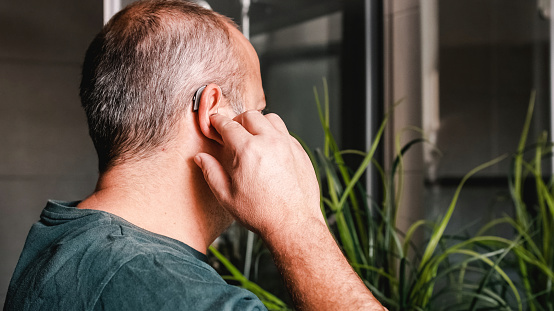 Man holding hearing aid against side of head - image is from the rear and side