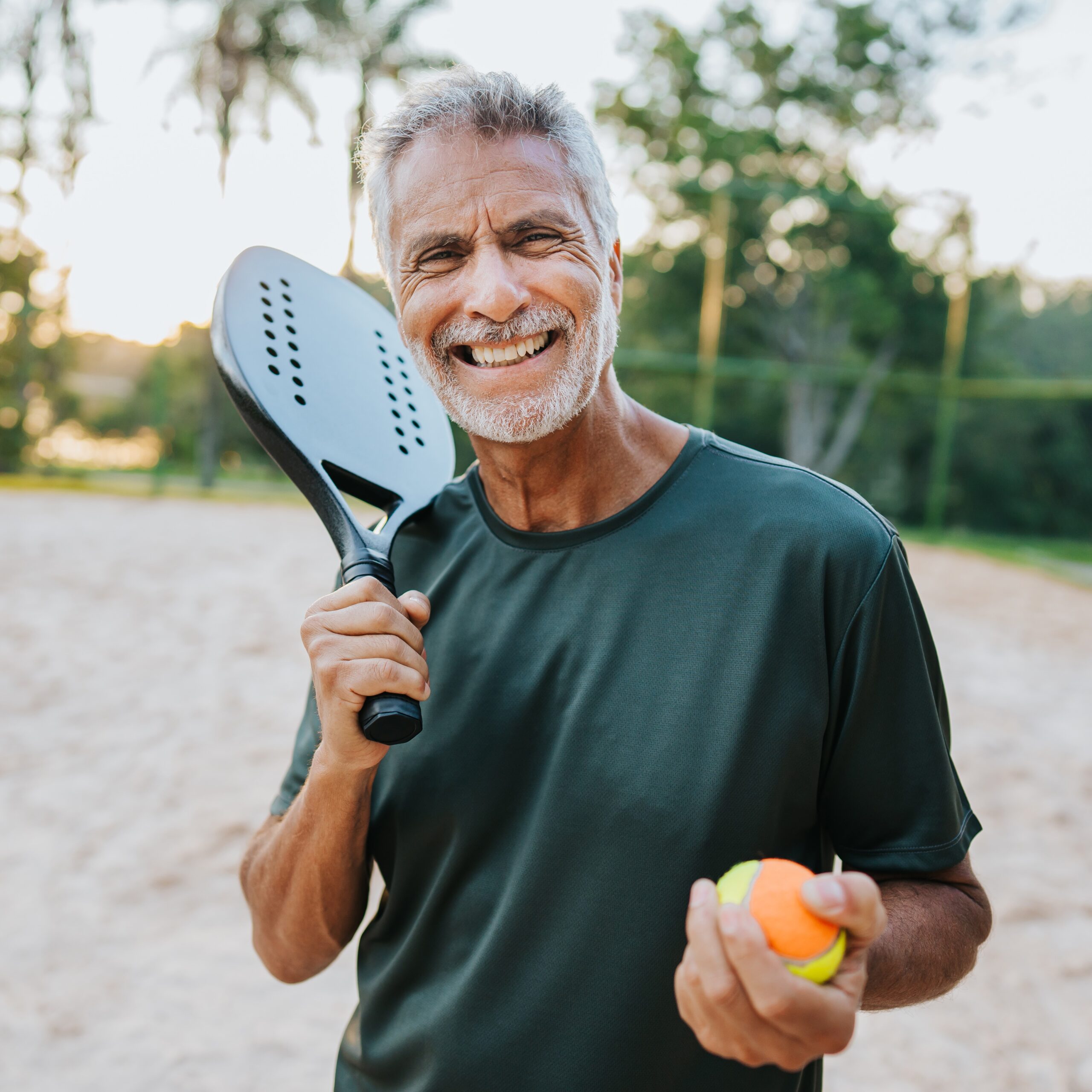Smiling active older person holding a pickleball mallet and ball.